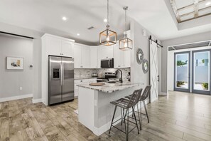 A modern kitchen with white cabinetry, stainless steel appliances, and a central island with bar stools. - Kid-Friendly Bonita Home With Private Pool & Spa (Bonita Springs)