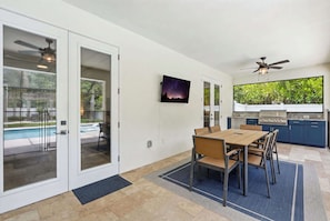 A modern kitchen with a built-in grill, a dining area with a table and chairs, and a pool visible through glass doors. - Kid-Friendly Bonita Home With Private Pool & Spa (Bonita Springs)