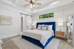 Une chambre à coucher comprenant un lit, des tables de chevet, un ventilateur de plafond, une fenêtre avec vue et une porte.