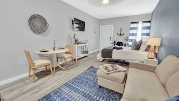 A modern living room with a sofa, a dining table with chairs, a TV mounted on the wall, and a ceiling fan.