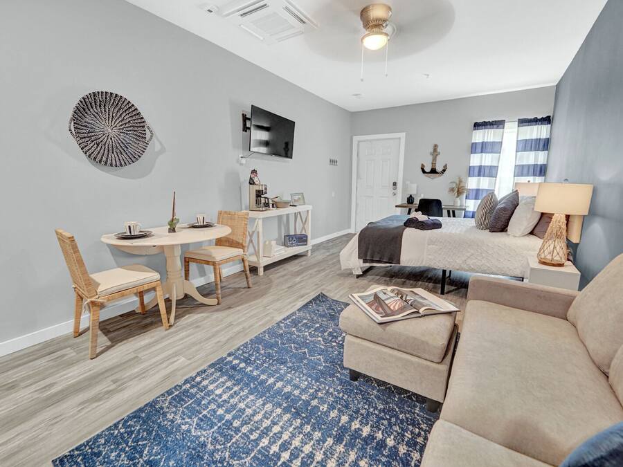 A modern living room with a sofa, a dining table with chairs, a TV mounted on the wall, and a ceiling fan.