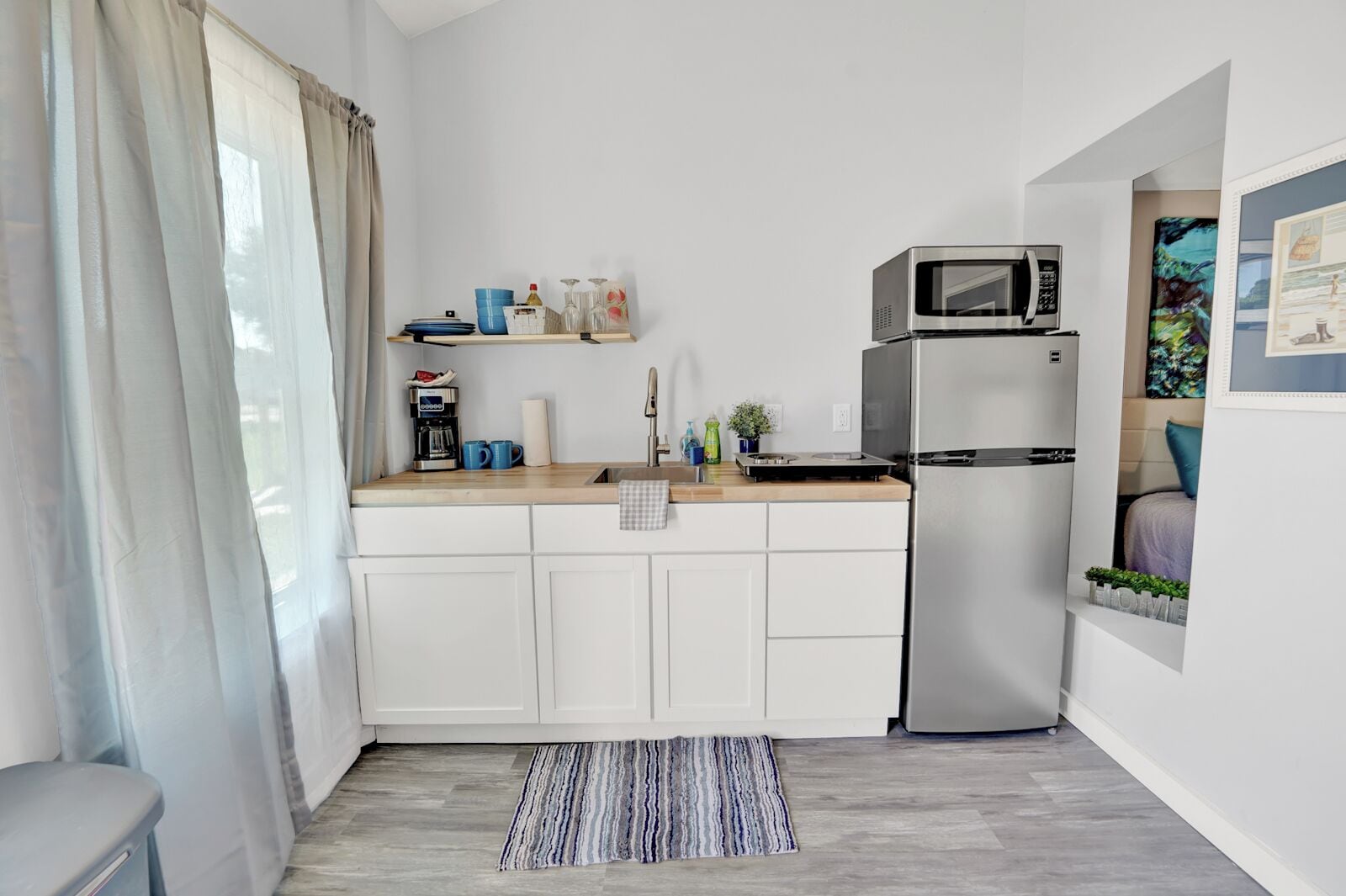Cocina compacta con armarios blancos, refrigerador de acero inoxidable, microondas y cafetera.
