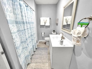 A bathroom with a shower curtain, toilet, sink, and a mirror. - Seaside Escape FL (Fort Walton Beach)