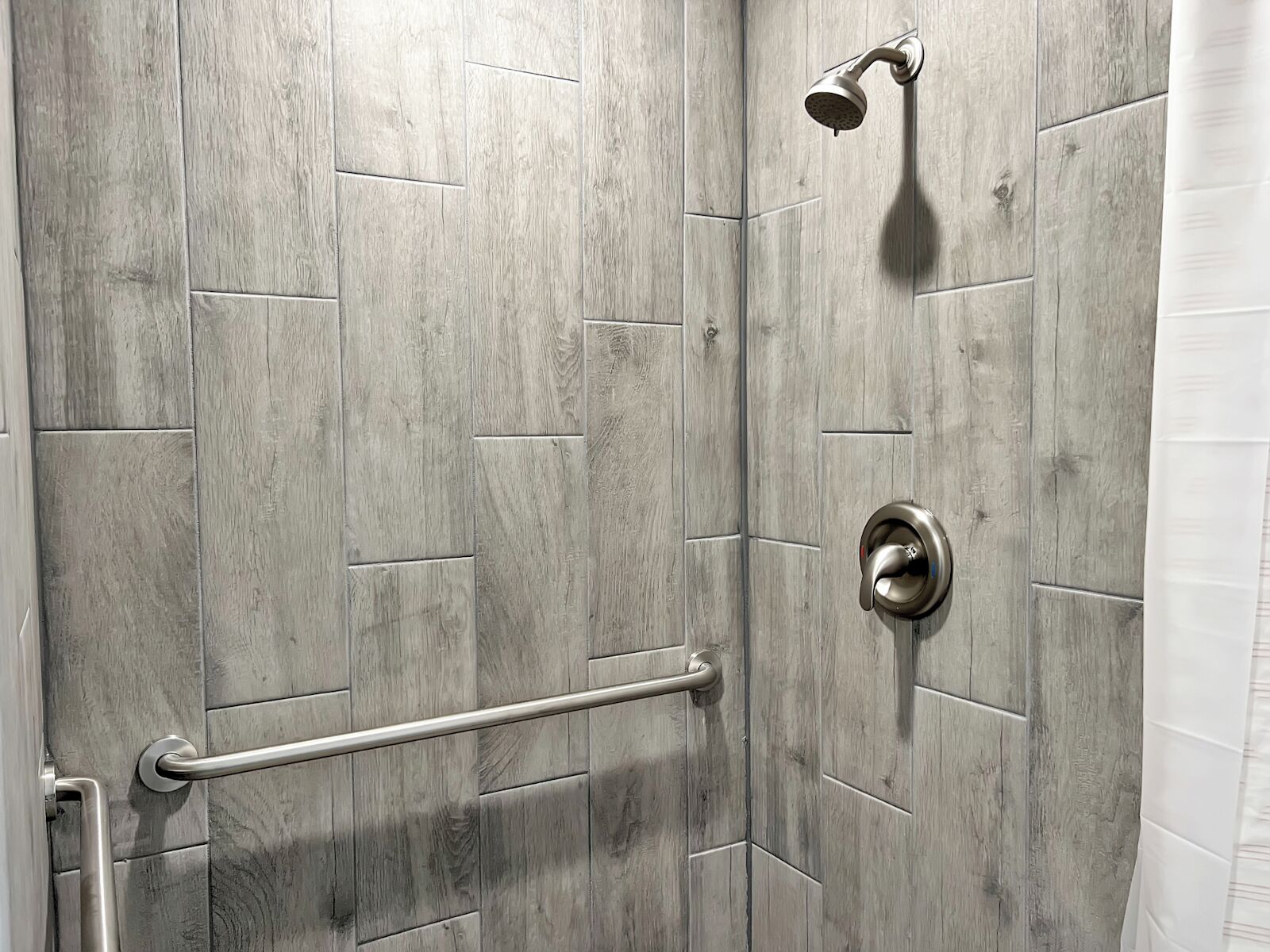 A shower area with a wooden wall design, a handheld showerhead, and a grab bar.