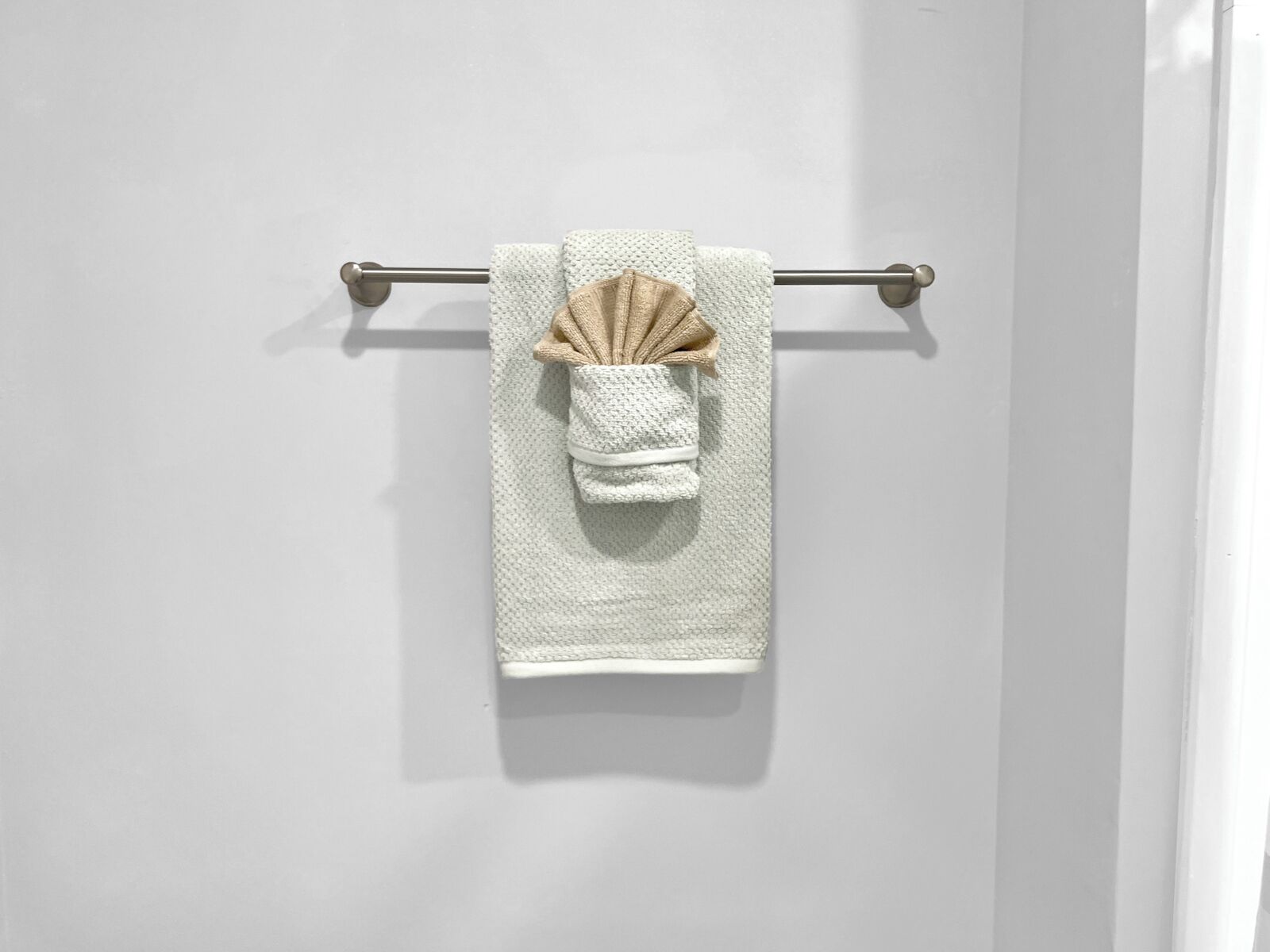 Une serviette blanche ornée d’un nœud décoratif marron, suspendue à une barre à serviettes en métal, le tout adossé à un mur blanc.