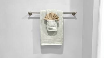 Une serviette blanche ornée d’un nœud décoratif marron, suspendue à une barre à serviettes en métal, le tout adossé à un mur blanc.