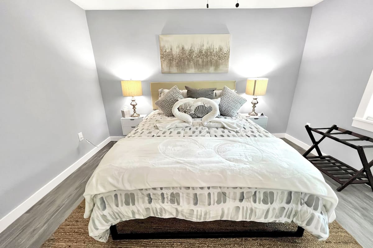 A modern bedroom with a large bed, two bedside lamps, a wall-mounted artwork, and a unique chair design.