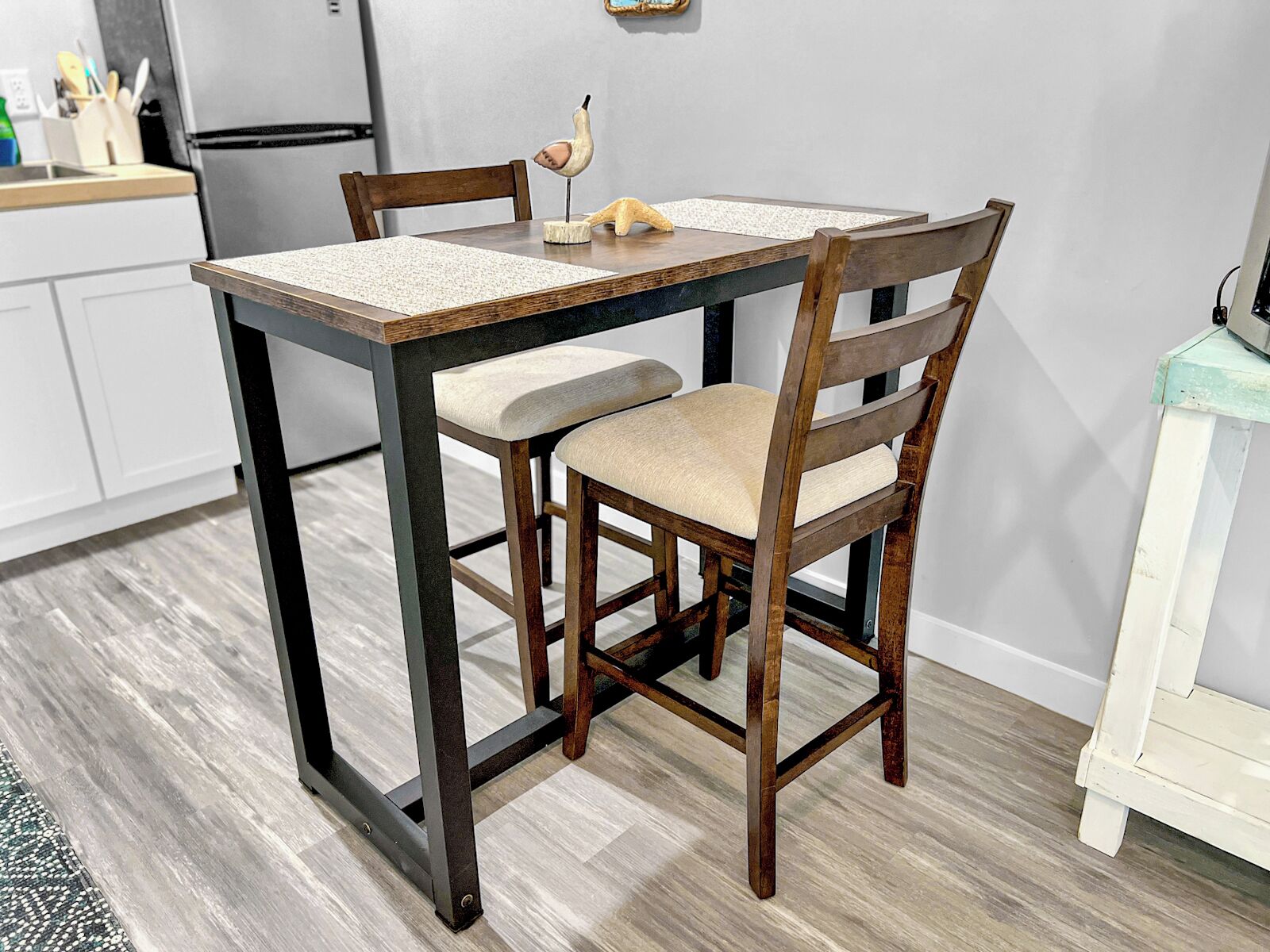 Une table à manger avec des chaises, un coin cuisine avec des placards et un réfrigérateur.