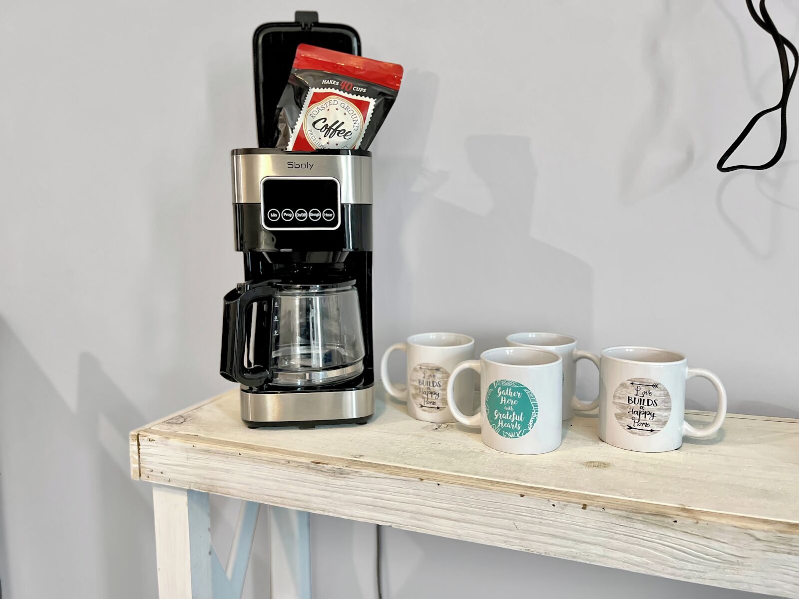 Una cafetera con una cápsula de café sobre una mesa de madera, acompañada de cuatro tazas con frases motivacionales.