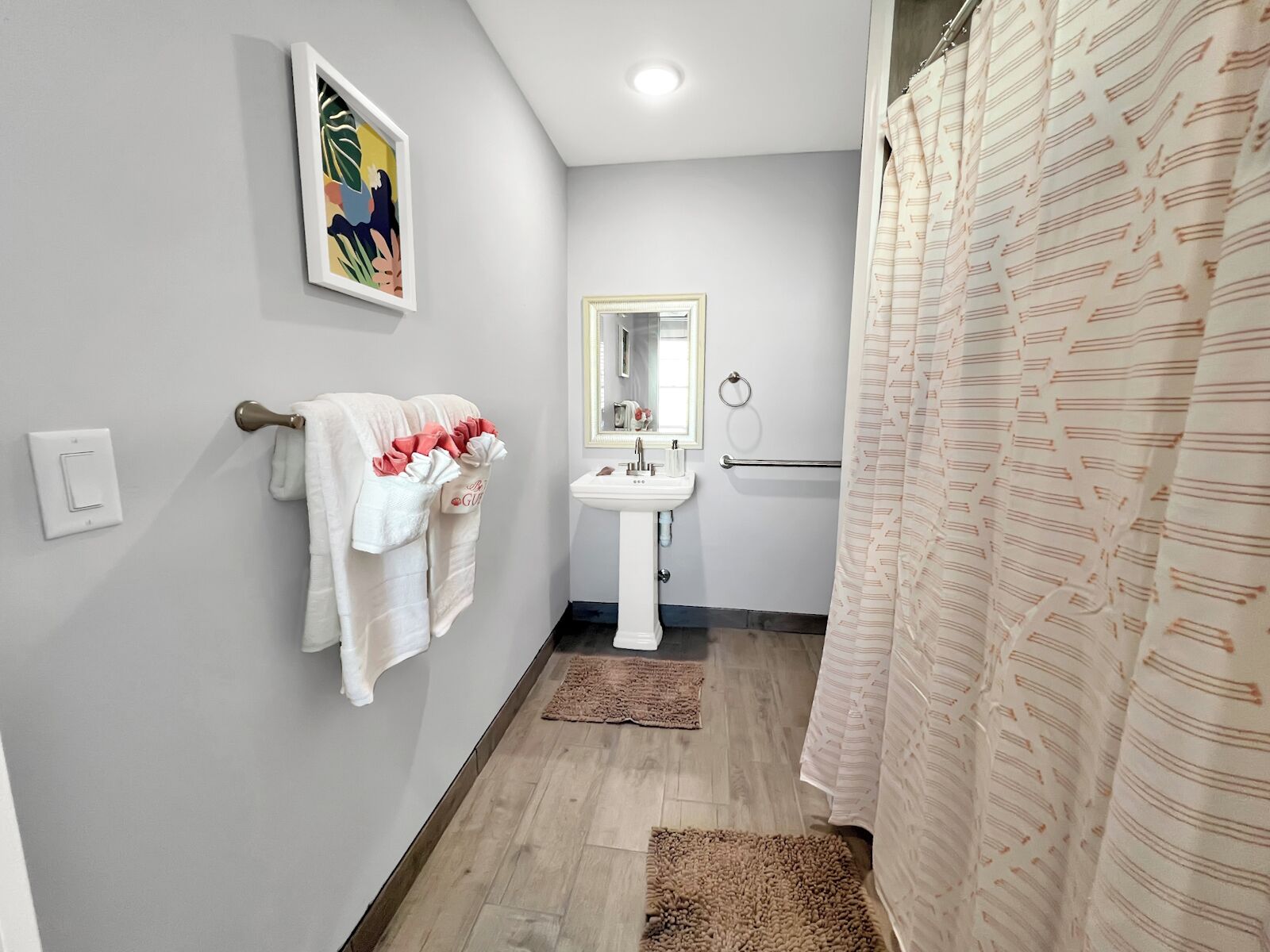 Une salle de bain avec un lavabo blanc, un miroir, un porte-serviettes avec des serviettes, un rideau de douche et un plancher en bois.