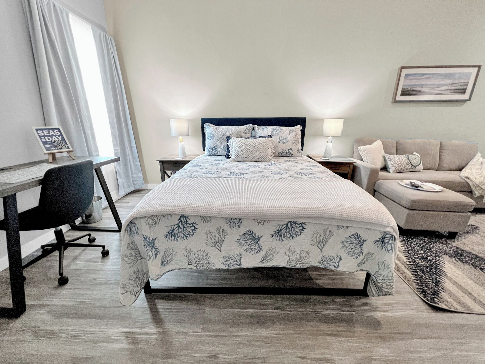 A hotel room with a bed, a desk, a chair, a sofa, and a rug.