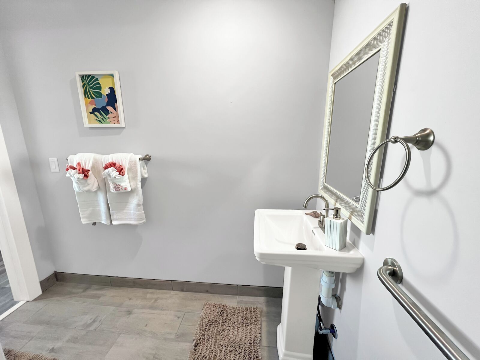 Un baño con un lavamanos blanco, un espejo y dos toallas colgadas en la pared.