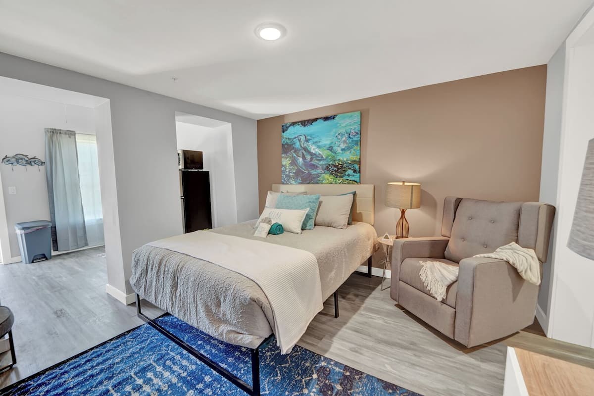A modern hotel room with a bed, a chair, a desk, and a painting on the wall.