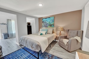 Una habitación de hotel moderna con una cama, una silla, un escritorio y un cuadro en la pared.