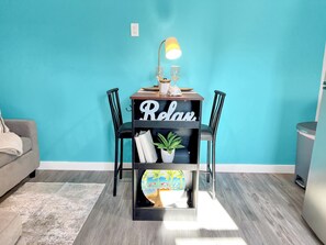 A teal-walled room with a black bookshelf labeled 'Relax,' a lamp, and a small potted plant.