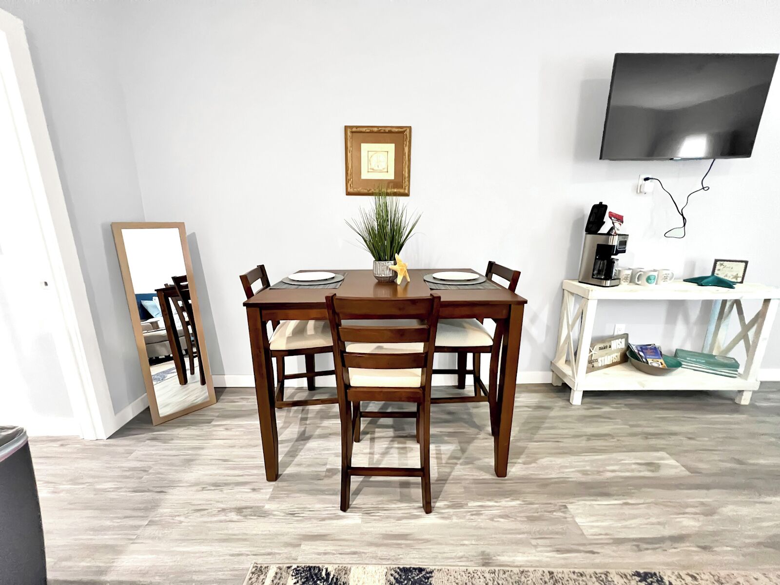 A dining area with a wooden table, chairs, a potted plant, and a television mounted on the wall.
