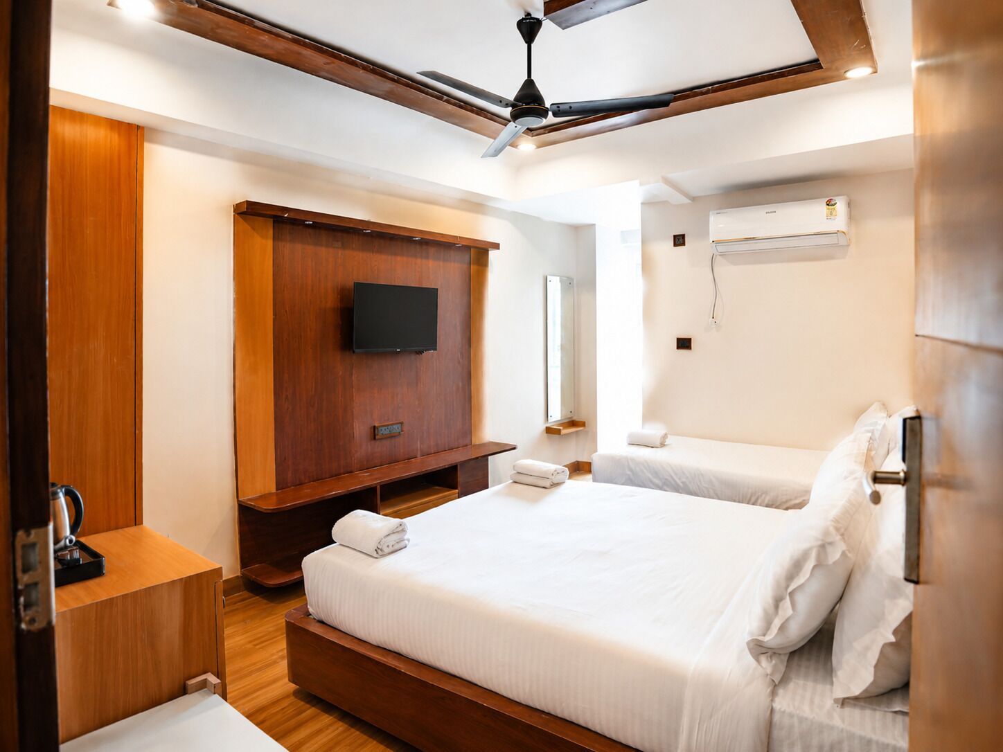 Habitación de hotel con cama de madera, televisor de pantalla plana, ventilador de techo y aire acondicionado.