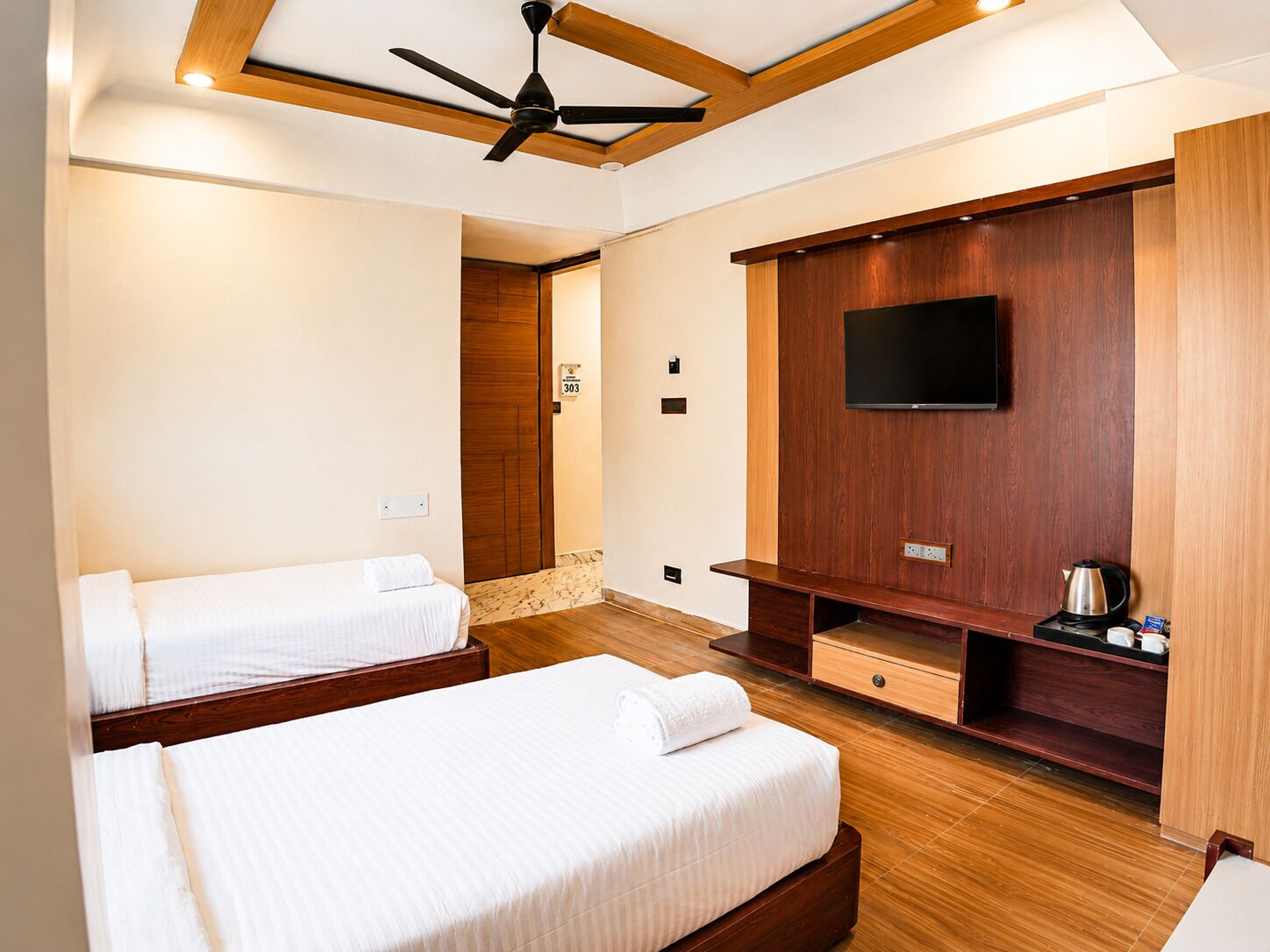 A hotel room with two beds, a ceiling fan, a TV mounted on a wooden panel, and a coffee maker on the sideboard.