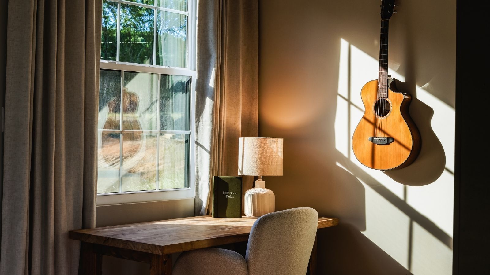 Una habitación con ventana, una guitarra, una lámpara y una silla.