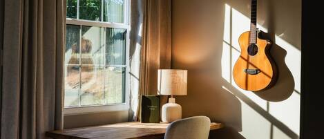 Una habitación con ventana, una guitarra, una lámpara y una silla.