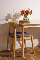 Una silla de madera con cojín, una mesa de madera y un jarrón con flores rojas.