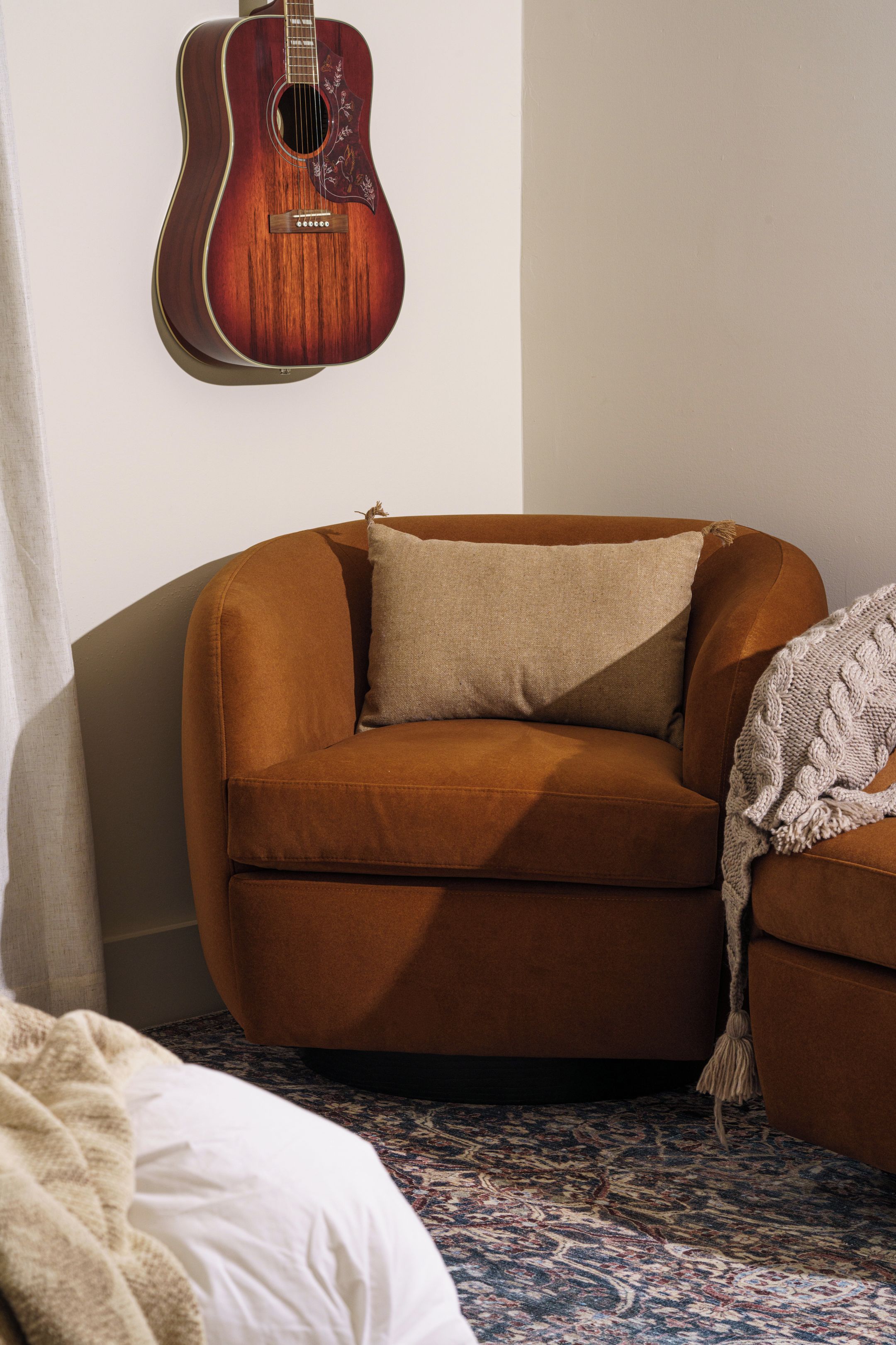 A room with a brown sofa, a white blanket, and a guitar on the wall.