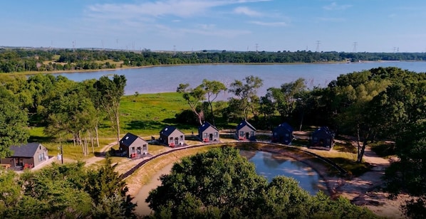 A lakeside property with multiple cabins, a dirt path, and a small bridge connecting the cabins.
