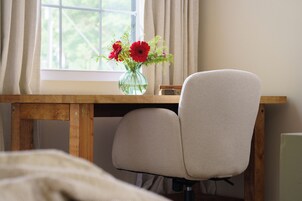 Un escritorio de madera con un jarrón de flores, una silla y una ventana con cortinas.