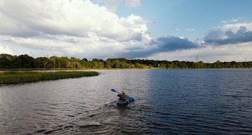 Una persona haciendo kayak en aguas tranquilas, con una orilla boscosa y un cielo nublado.