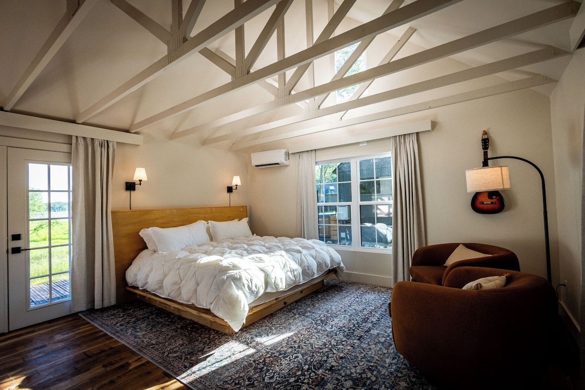 A bedroom with a wooden bed, a brown armchair, and a guitar on the wall.