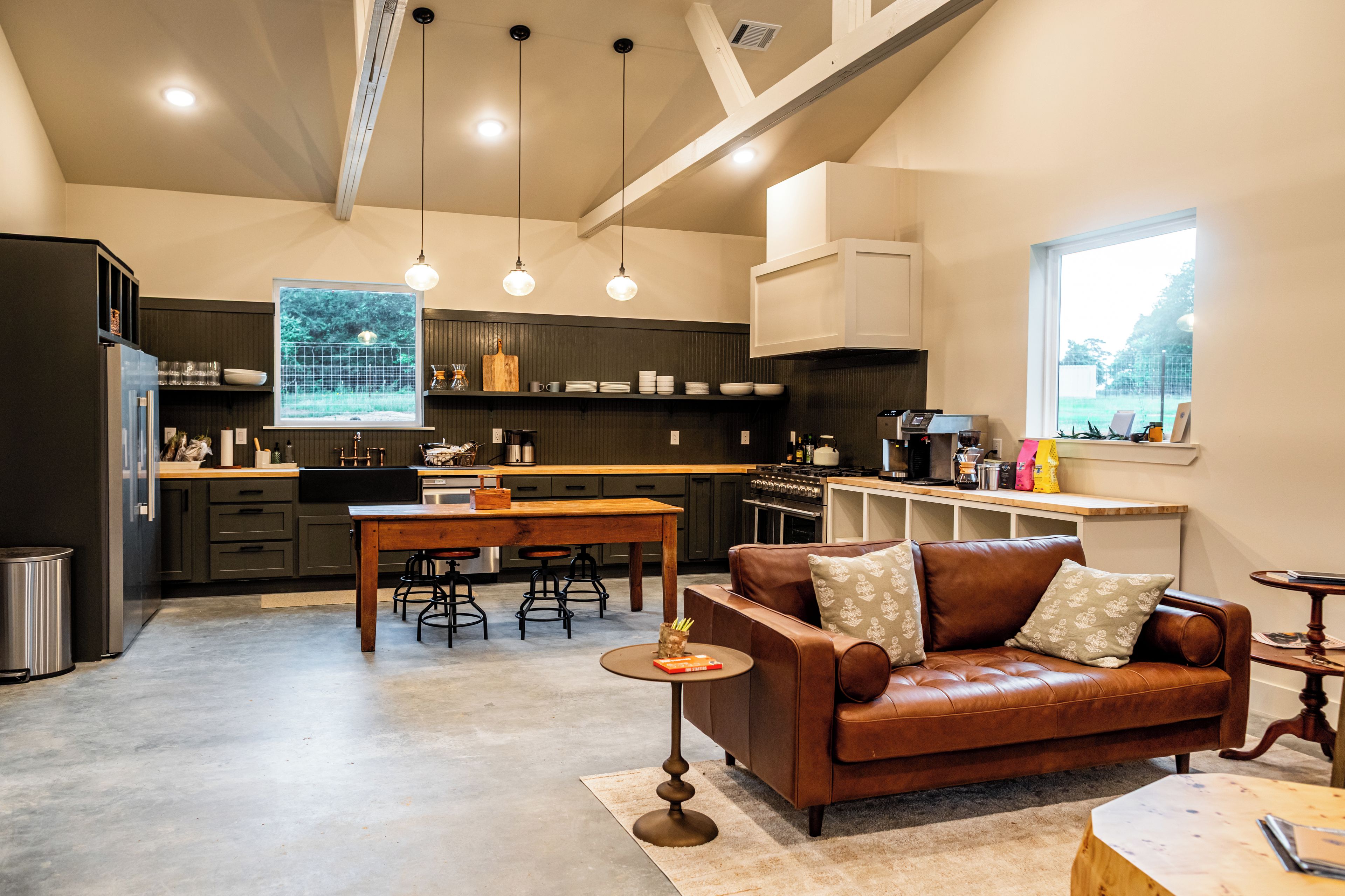 A modern kitchen with a dining area, a leather sofa, and a large window.
