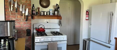 A kitchen with a gas stove, a red kettle, a white refrigerator, and various kitchen utensils and appliances.
