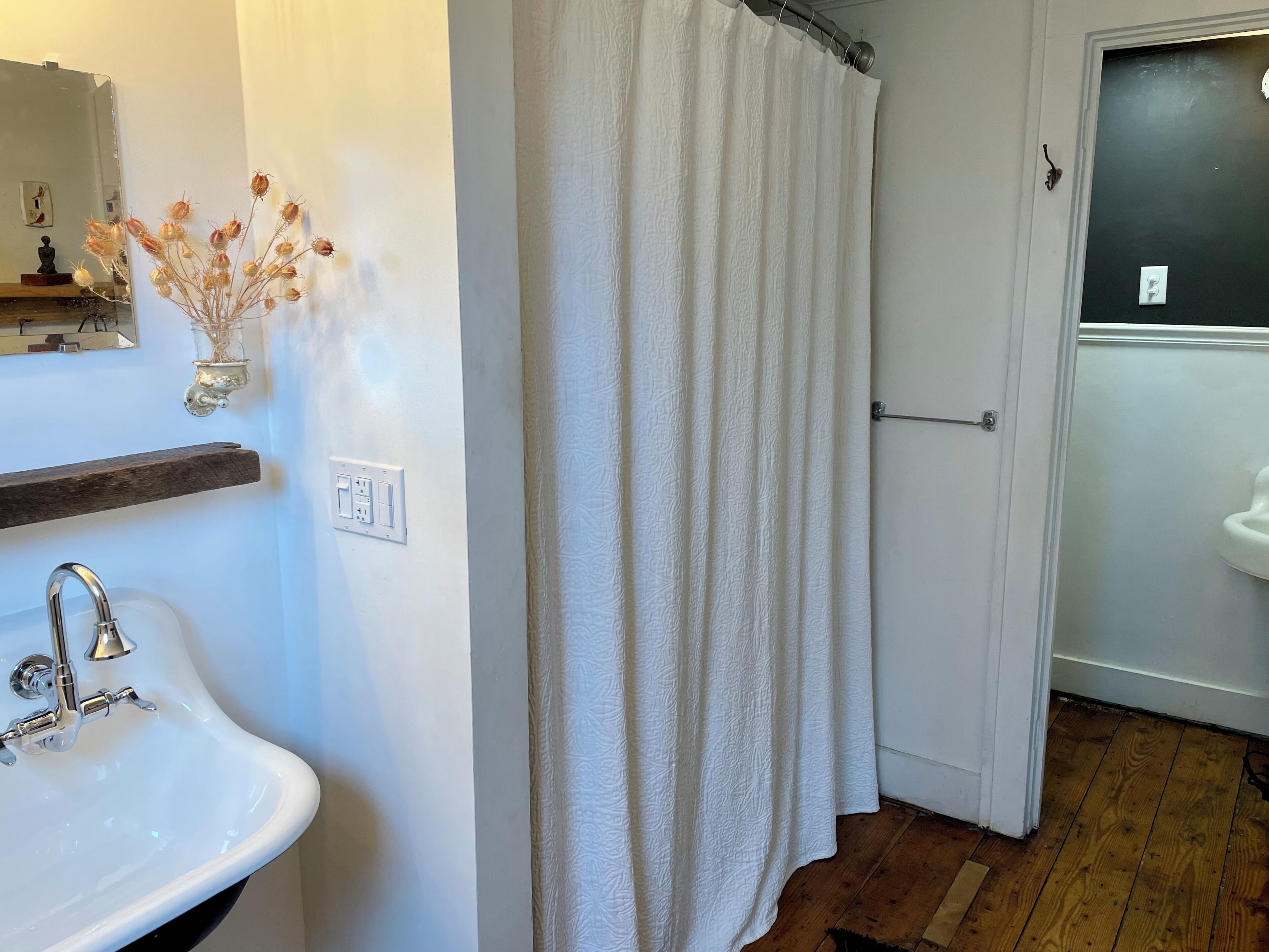 A bathroom with a white sink, a shower curtain, and a wooden floor.