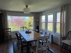 A dining room with a long wooden table, several chairs, a ceiling fan, and large windows with curtains. - Charming 1830s Farmhouse (Interlaken)