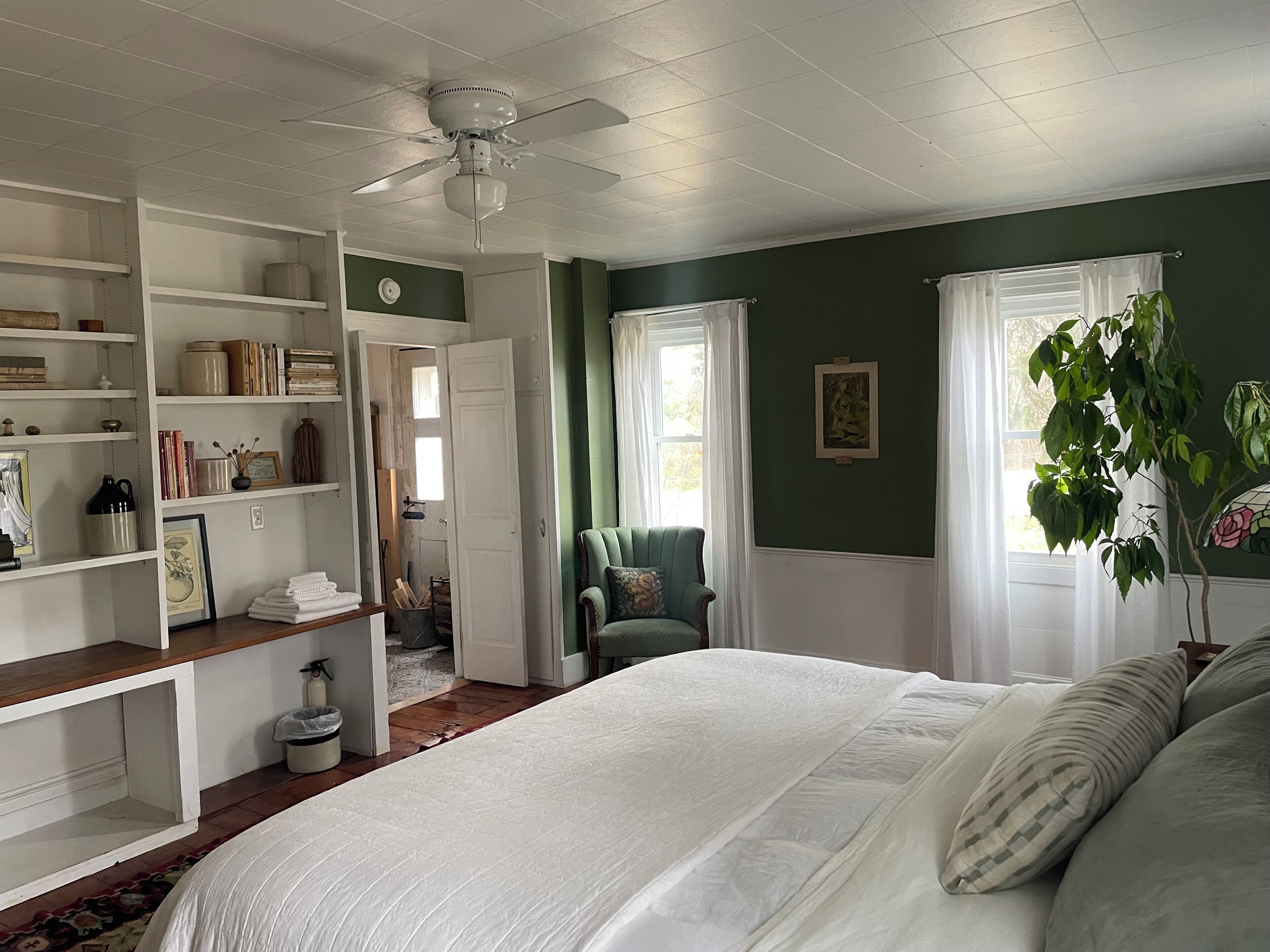 A bedroom with a bed, a ceiling fan, a green wall, and a window with curtains.
