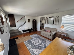 A living room with hardwood flooring, a sofa, a coffee table, a rug, a bench, a staircase, and a dining area. - 3-bedroom bungalow in peaceful Fenton in the Shiawassee River! (Fenton)