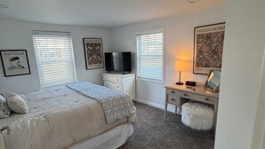Un dormitorio con una cama, un escritorio, un televisor y obras de arte en las paredes.