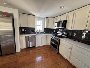 A kitchen with white cabinets, stainless steel appliances, and a wooden floor. - 3-bedroom bungalow in peaceful Fenton in the Shiawassee River! (Fenton)