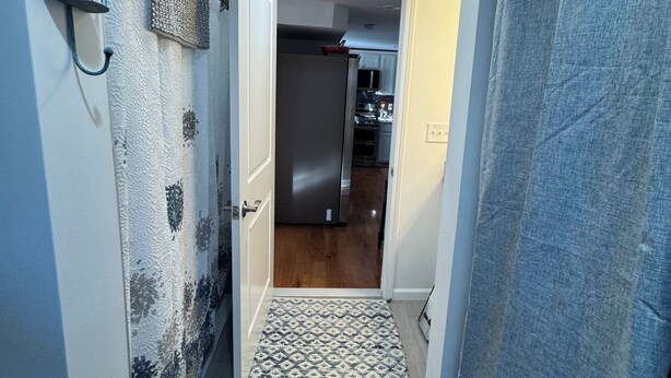 Un pasillo con un tapete estampado, una puerta que da a una cocina y una cortina de ducha.