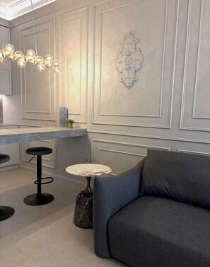 A modern interior with a grey sofa, a round table, and a bar area with stools.