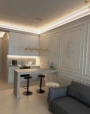 A modern kitchen with a central island, bar stools, and a grey sofa.