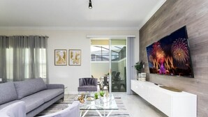 Una sala de estar moderna con un sofá gris, una mesa de centro de vidrio y un televisor de pantalla plana montado en una pared de madera.