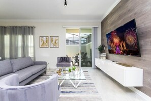 Ein modernes Wohnzimmer mit einem grauen Sofa, einem Glastisch und einem Flachbildfernseher, der an einer Holzwand angebracht ist.