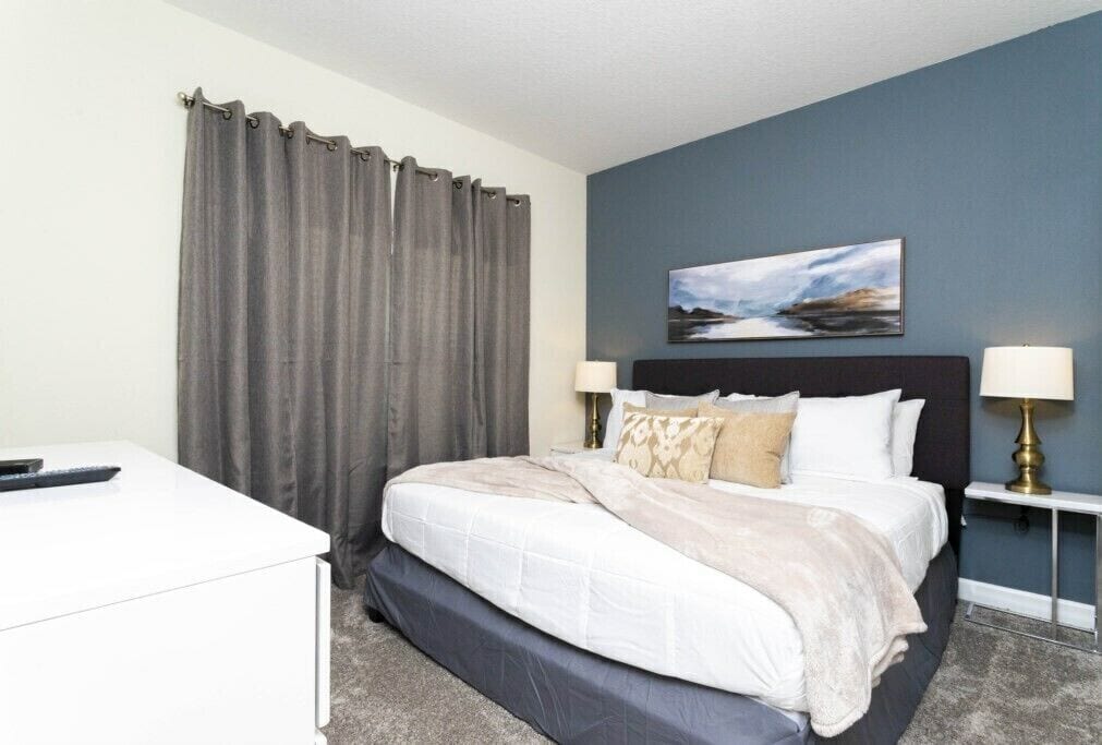 A hotel room with a bed, bedside lamps, a desk, and a painting on the wall.