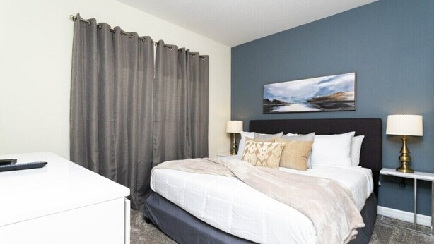 Una habitación de hotel con cama, lámparas de noche, escritorio y un cuadro en la pared.