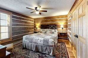 Ein Schlafzimmer mit einem Bett, einem Schreibtisch, einem Stuhl, einem Deckenventilator und Holzwänden.