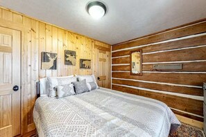 A wooden-paneled bedroom with a bed, wall-mounted artwork, and a plaque. - Fisher Haul Historic Lodge | Hot Tub & Riverfront (South Fork)