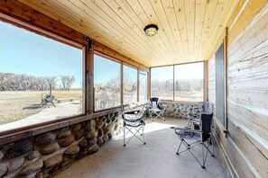 A covered porch with stone walls, large windows, and outdoor seating. - Fisher Haul Historic Lodge | Hot Tub & Riverfront (South Fork)