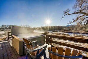 Ein Whirlpool auf einer Holzterrasse mit Stühlen, mit Blick auf eine verschneite Landschaft und einen klaren Himmel.