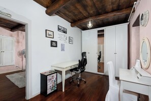 A room with a wooden ceiling, white walls, a desk with a chair, a mirror, and a dresser.